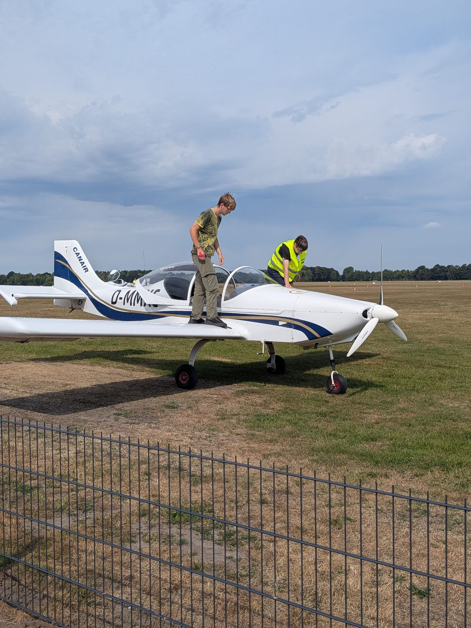 Two people checking a small aircraft on a grass airfield