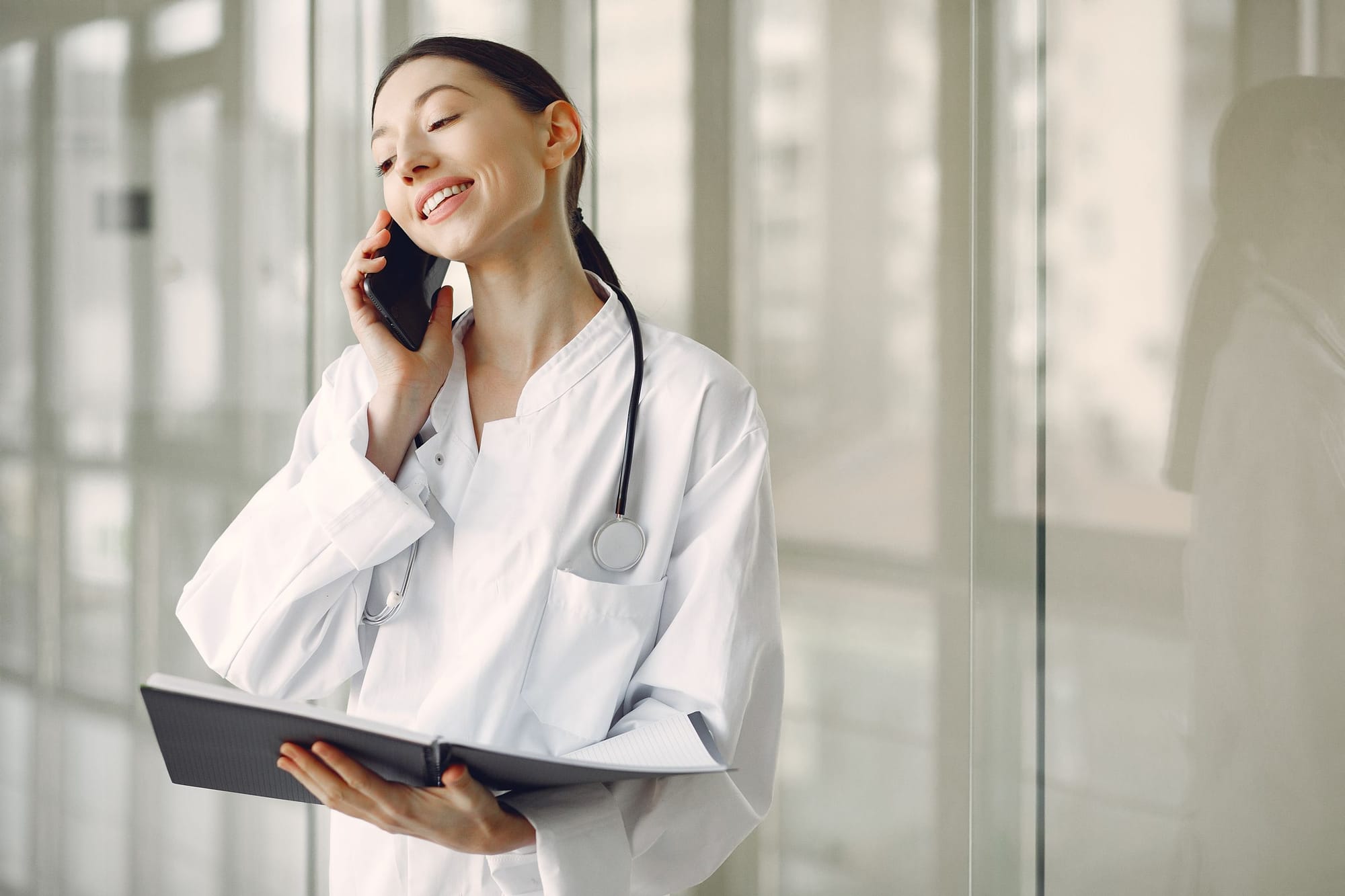 A smiling doctor on the phone in a bright hospital corridor