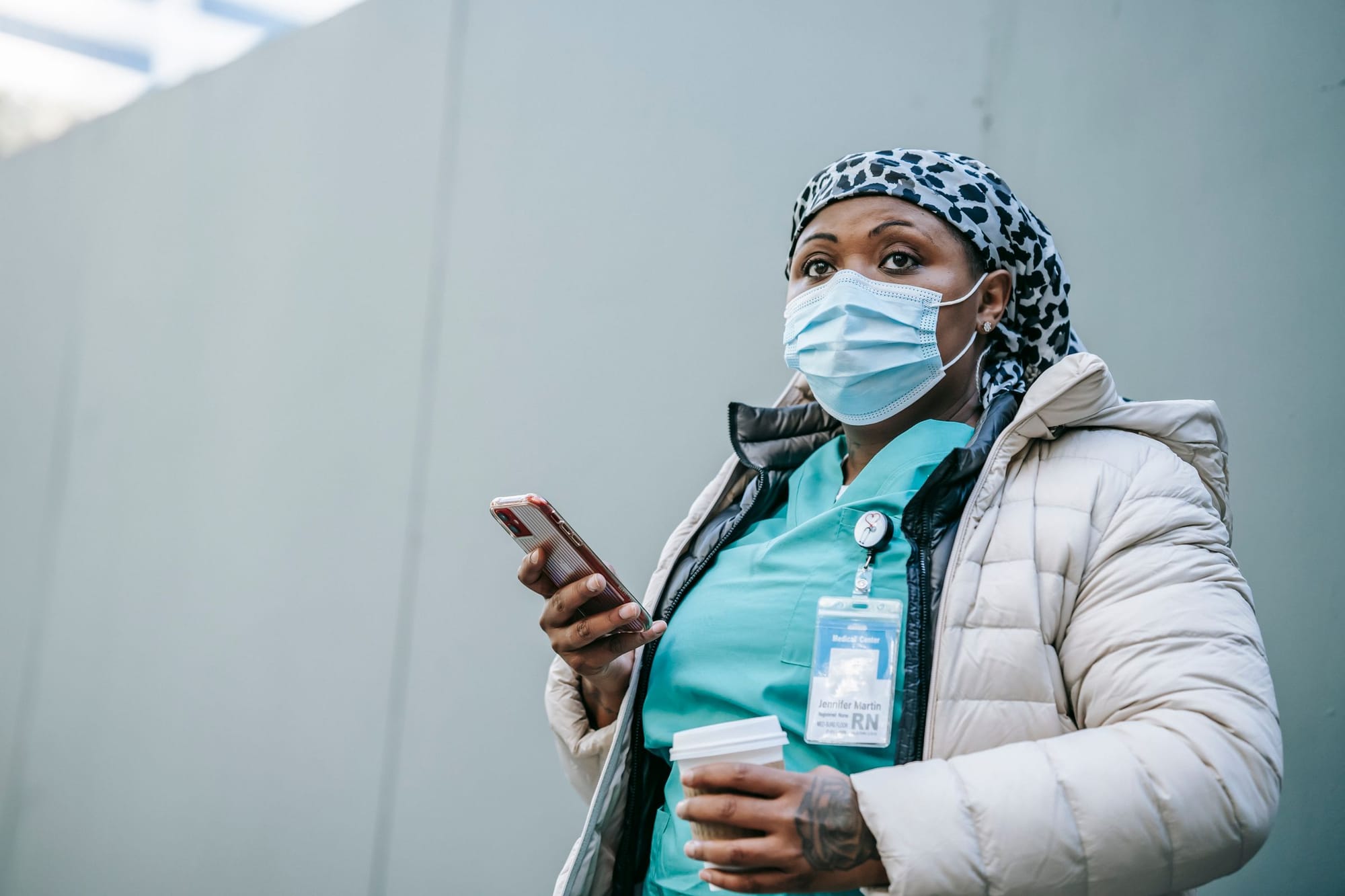 A nurse in a winter jacket checking her phone on the way to a shift