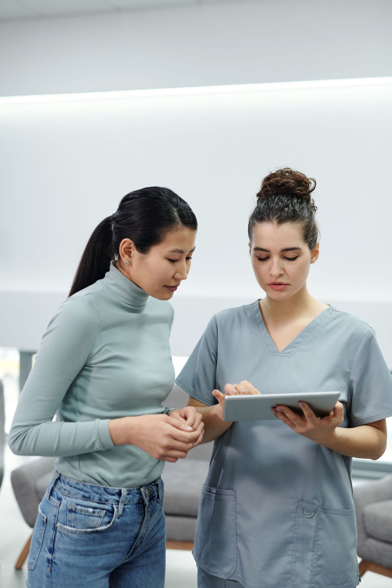 Two healthcare workers in scrubs looking at a tablet together