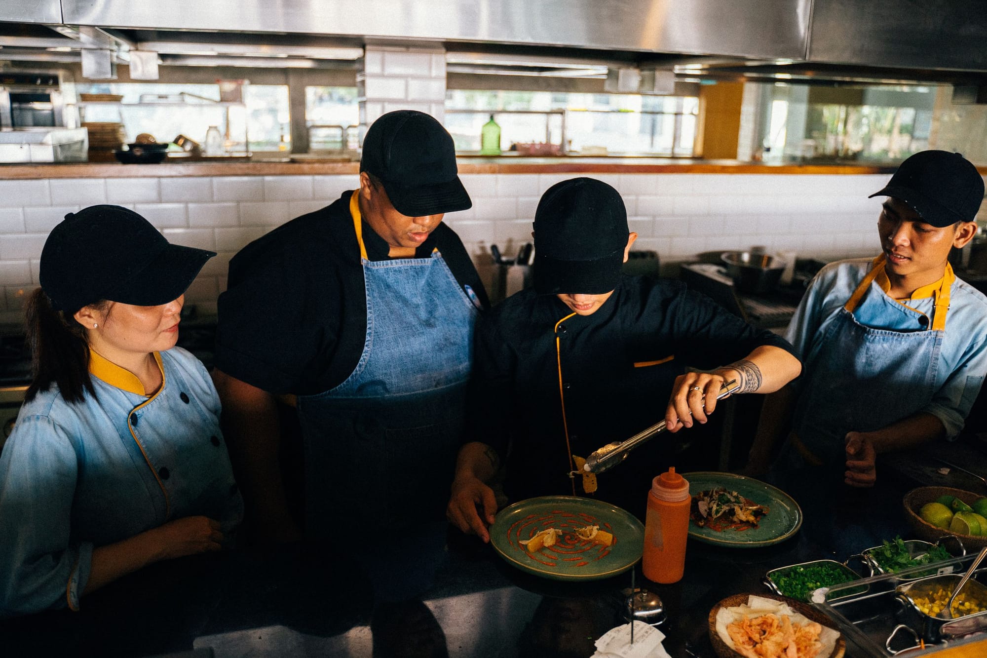 Chefs plating dishes together at the pass of a restaurant kitchen