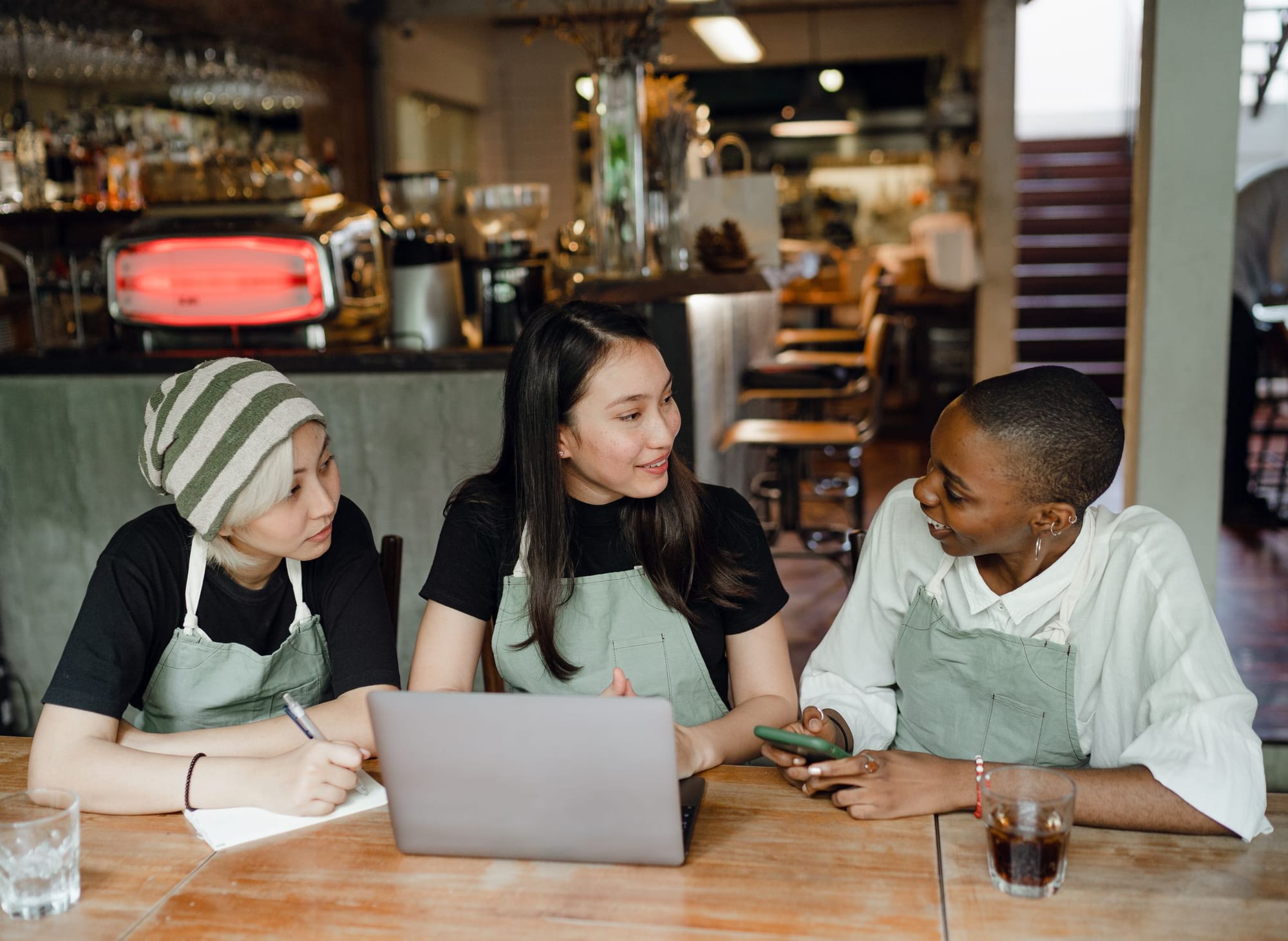 Three restaurant staff in aprons planning at a table with a laptop