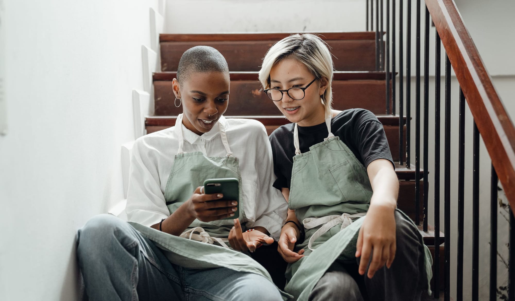 Two café staff in aprons looking at a phone on a break