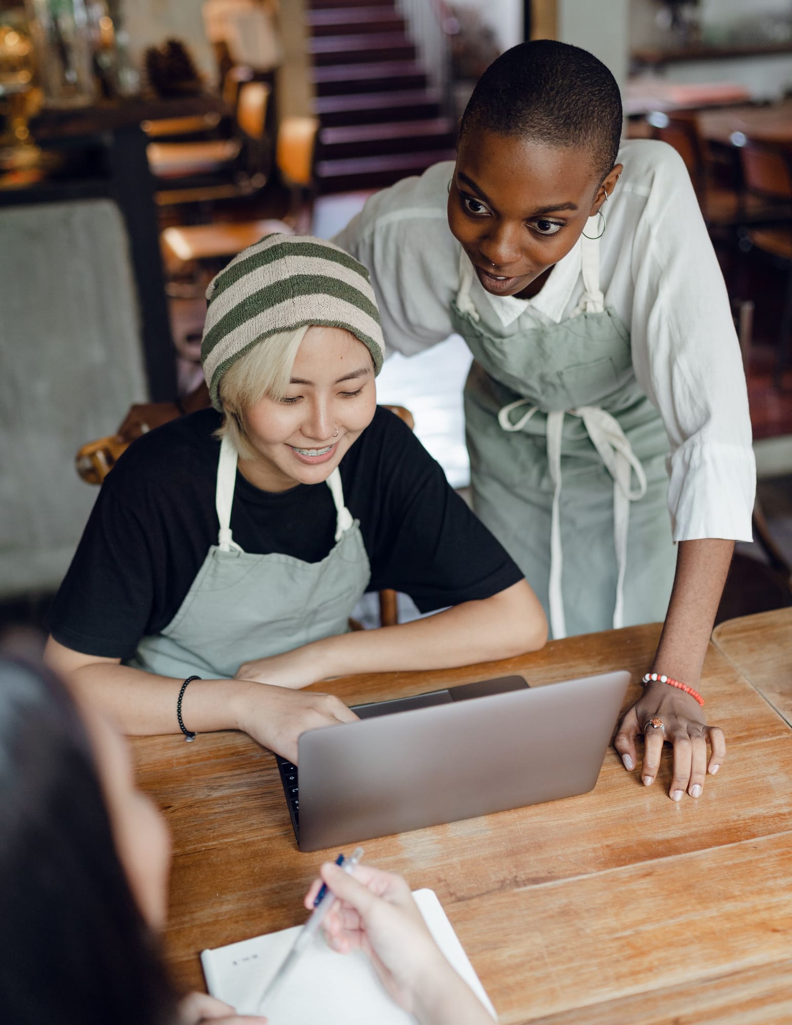 A café worker smiling at a laptop while a colleague looks on