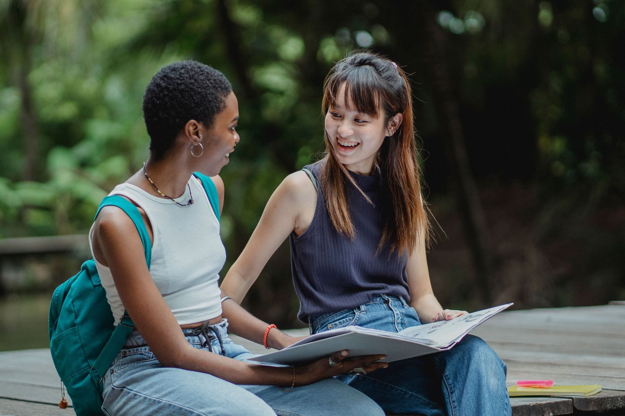 Two students laughing over a folder of notes outdoors