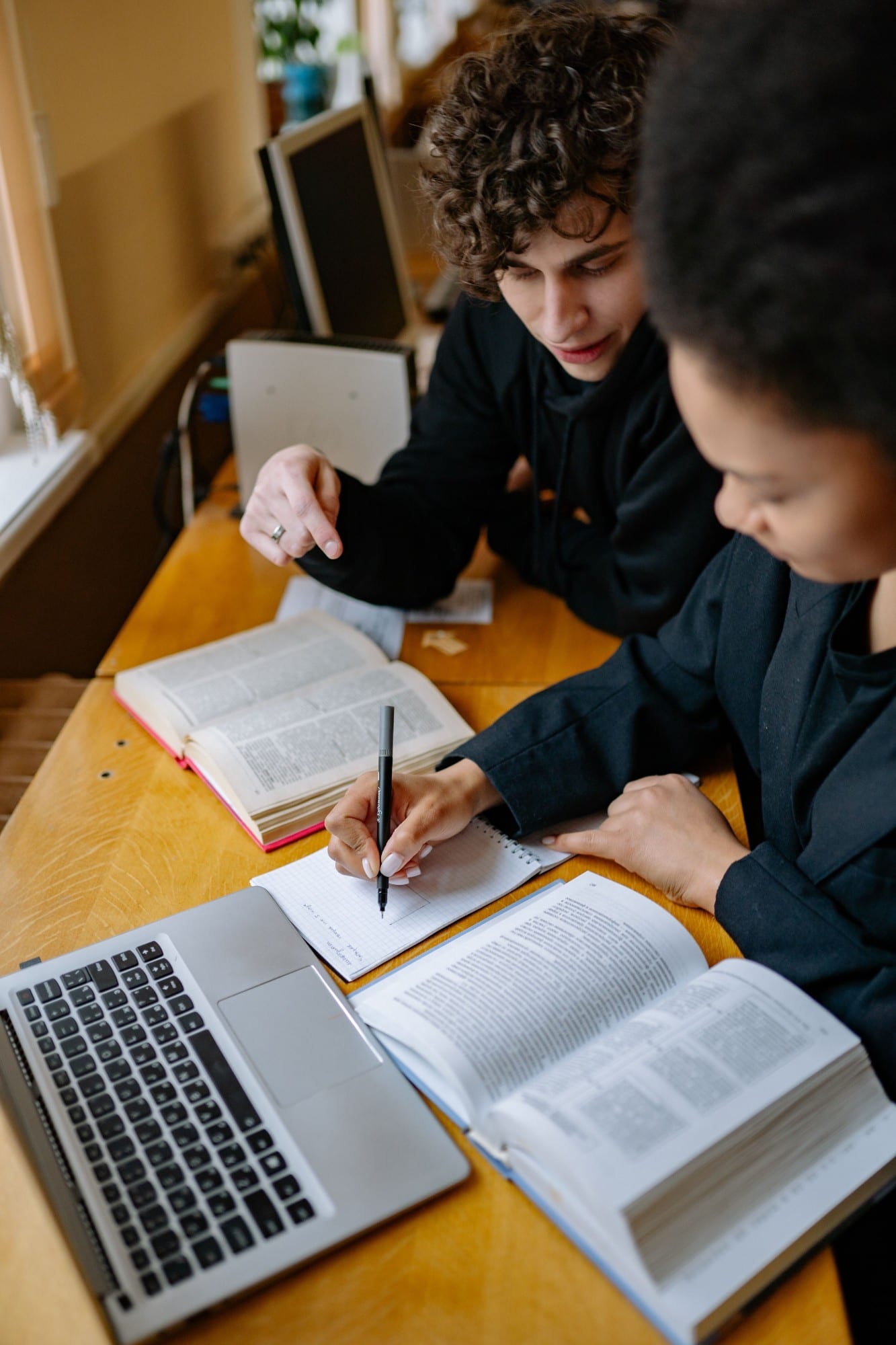 Two students taking notes beside a laptop and open books