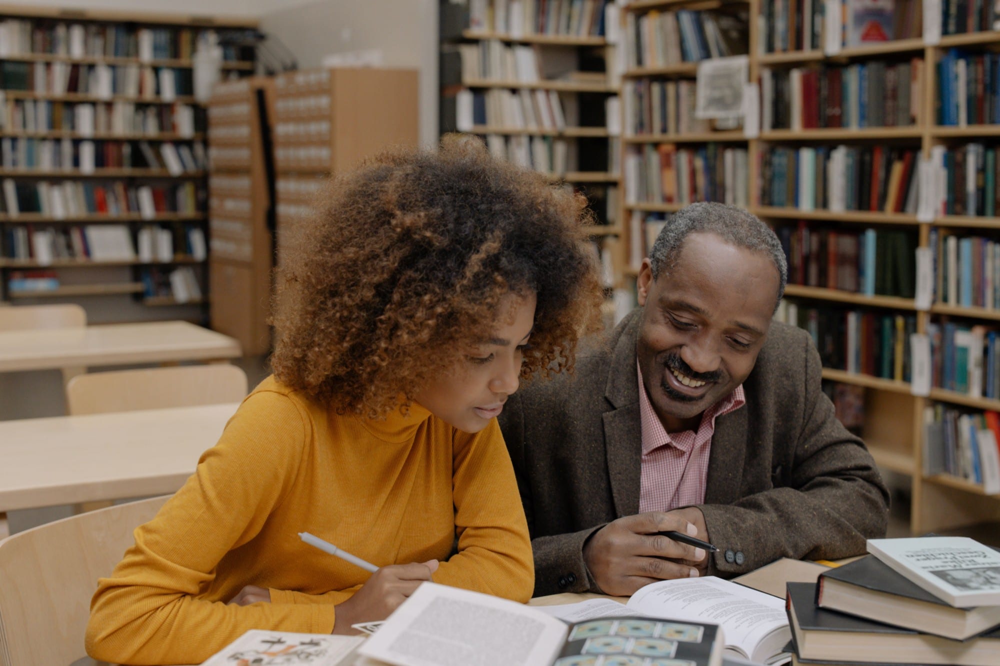 A tutor and a student reading together in a library